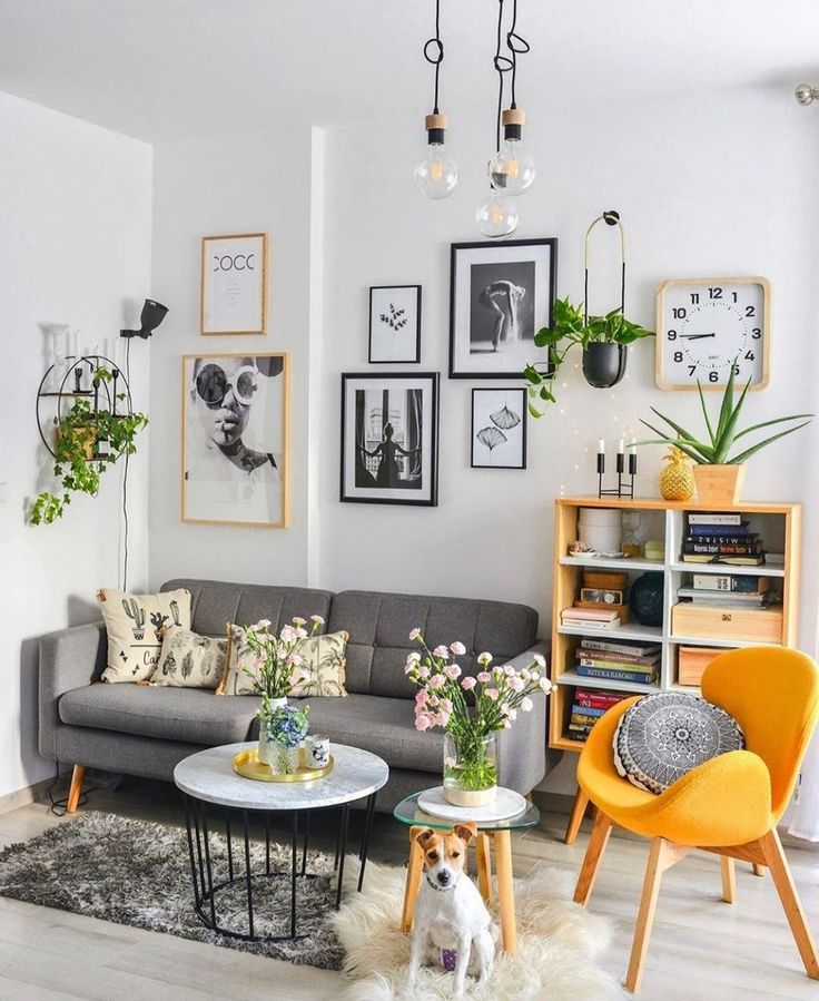 Sala com sofá cinza e pés de palito, parede branca com quadros e poltrona amarela