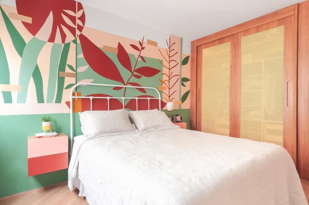 Quarto com cama de ferro branca, parede colorida de verde e bordô, roupeiro com telinha