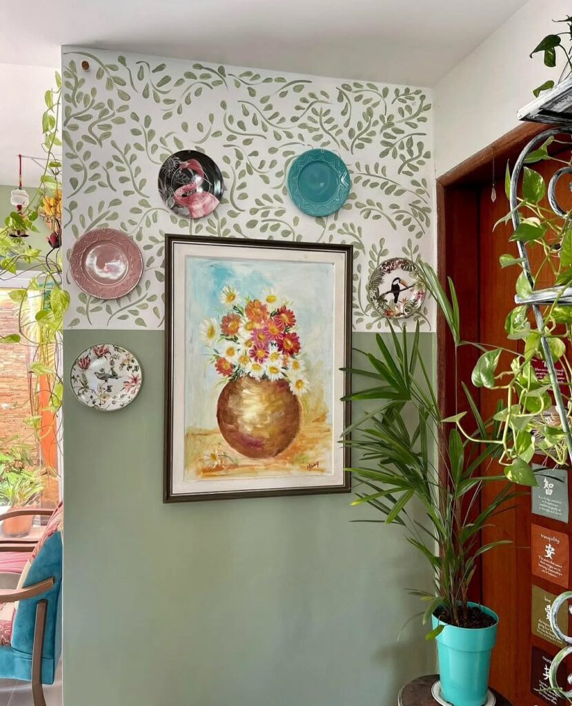 Parede pintada pela metade de um tom de verde e a outra parte de branco com folhinhas verdes decorada com pratos