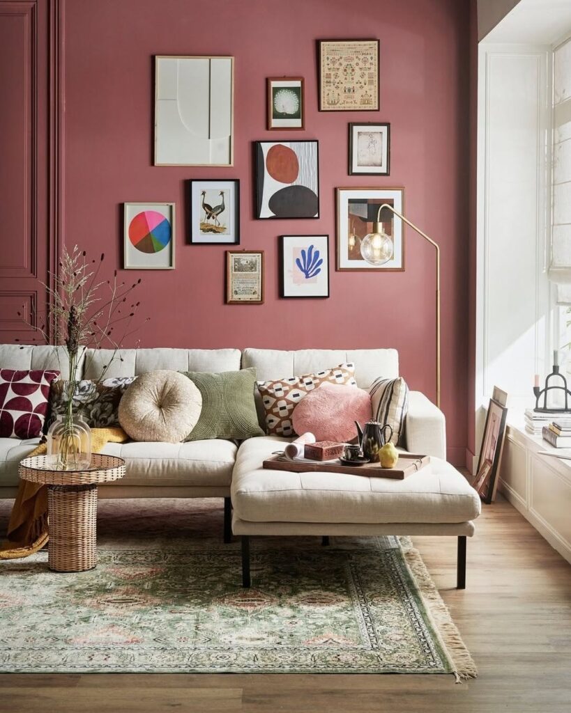 Sala de estar com sofá em cor neutra e parede atrás na cor rosa queimado com quadros