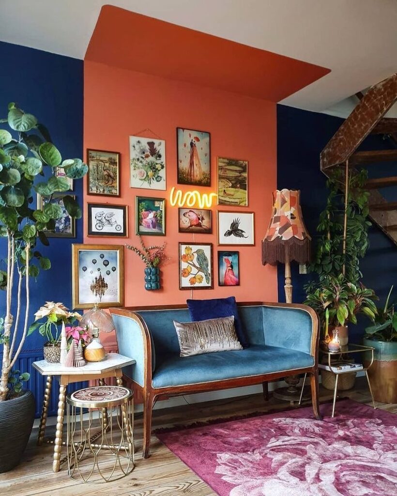 Sala de estar com sofá de madeira com estofado em veludo azul e paredes azuis e laranja com quadros