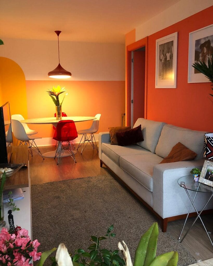 Sala de estar em jantar com sofá e mesa em tons neutros e paredes laranja