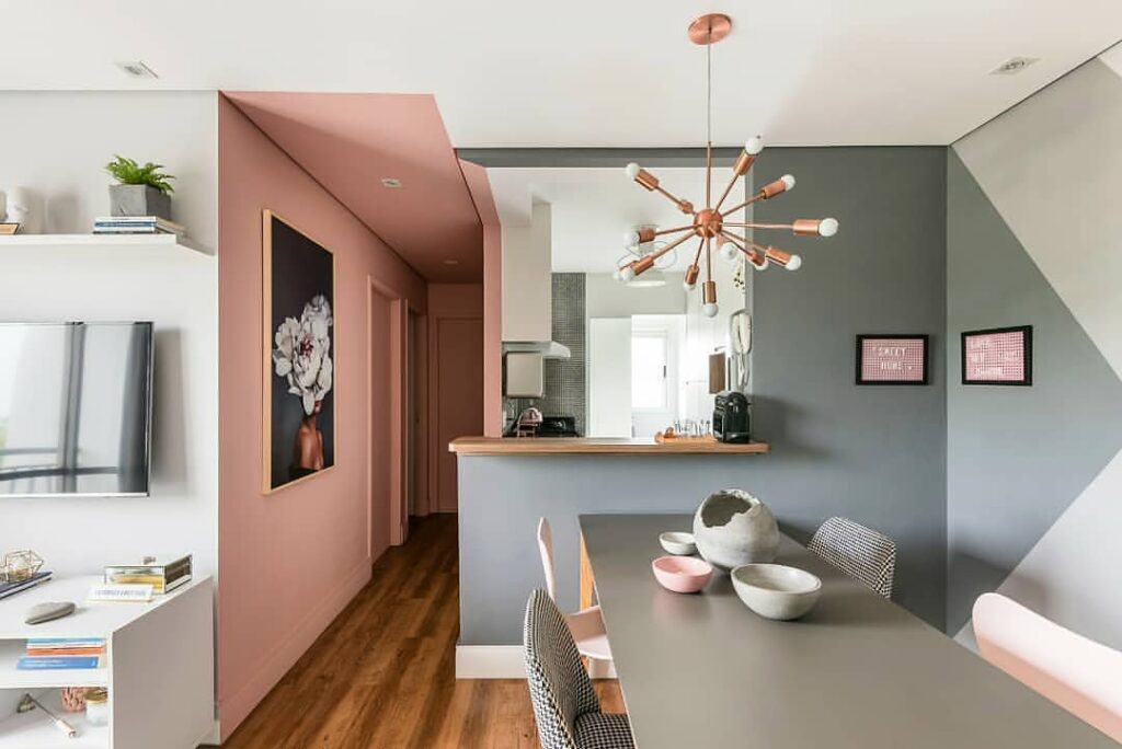 Sala de jantar com mesa cinza, pintura geométrica nas paredes e corredor em rosa