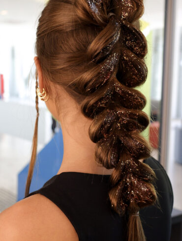 Mulher de pele clara de costas com cabelo trançado com glitter