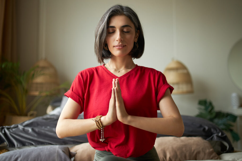 Mulher com camiseta vermelha e cabelo curto em posição de meditação