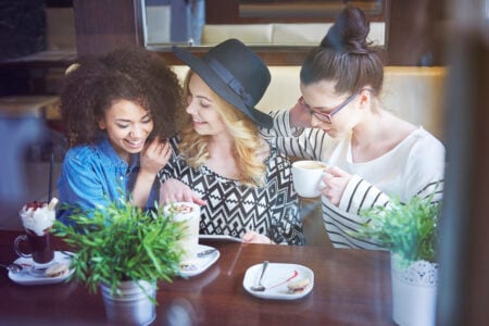 Três mulheres sentadas rindo em uma cafeteria