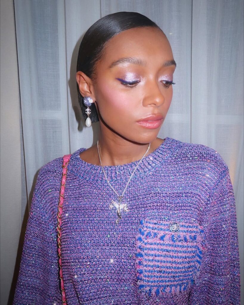 Mulher de pele preta, com blusa lilás e maquiagem em tons pastel