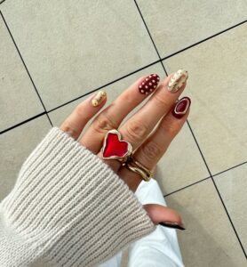 Mão de pele clara, com unha amendoada decorada com vermelho e dourado