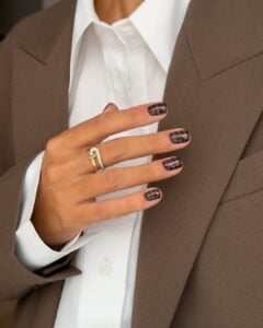 Mão de pele branca com esmalte marrom e nail art com estampa de cobra