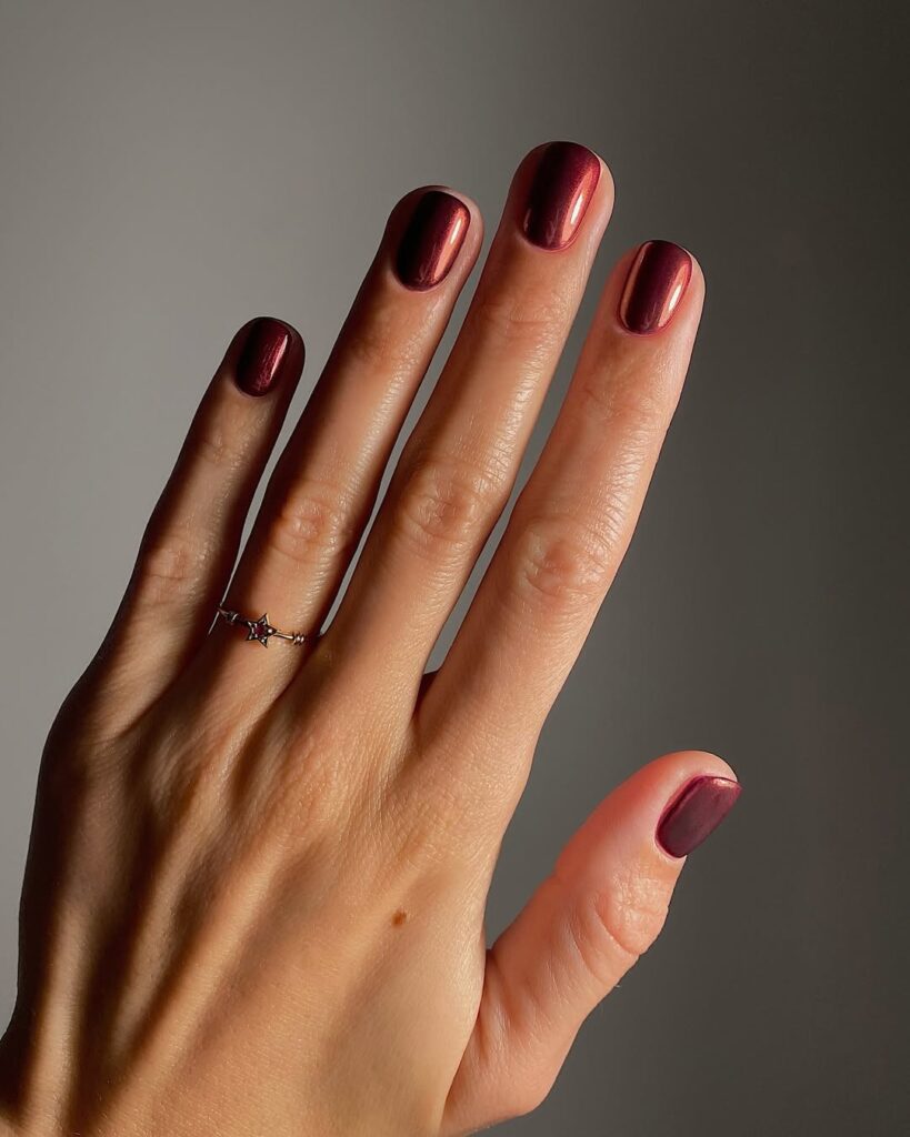 Mão de pele clara, com anel em dourado e vermelho e unha curta vermelho-cereja com acabamento cromado