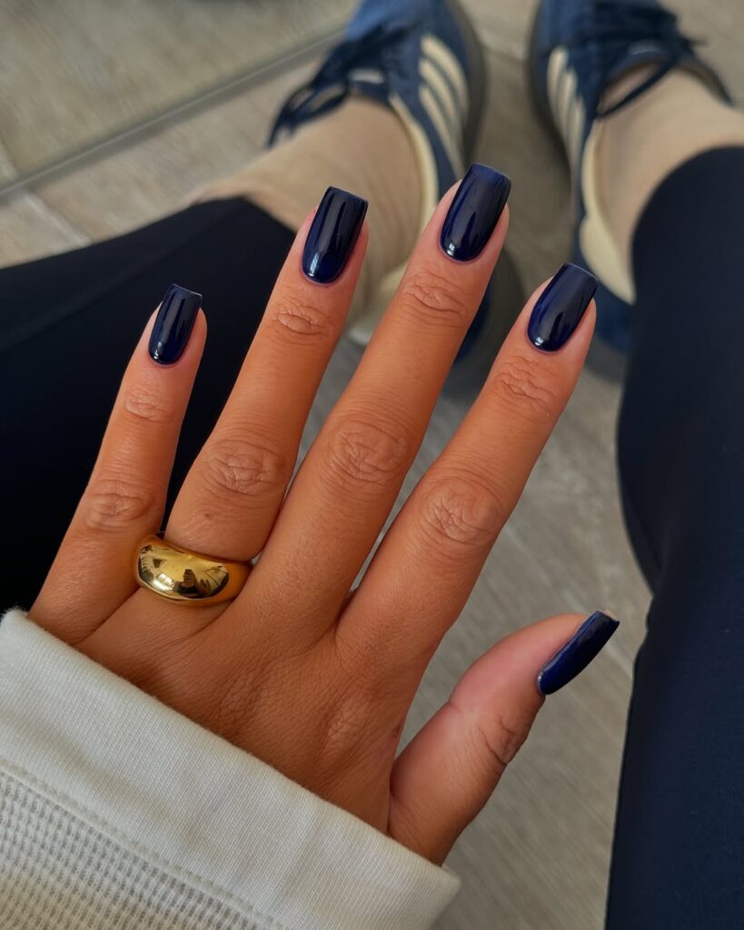 Mão de pele clara, com anel em dourado e unha quadrada azul-marinho