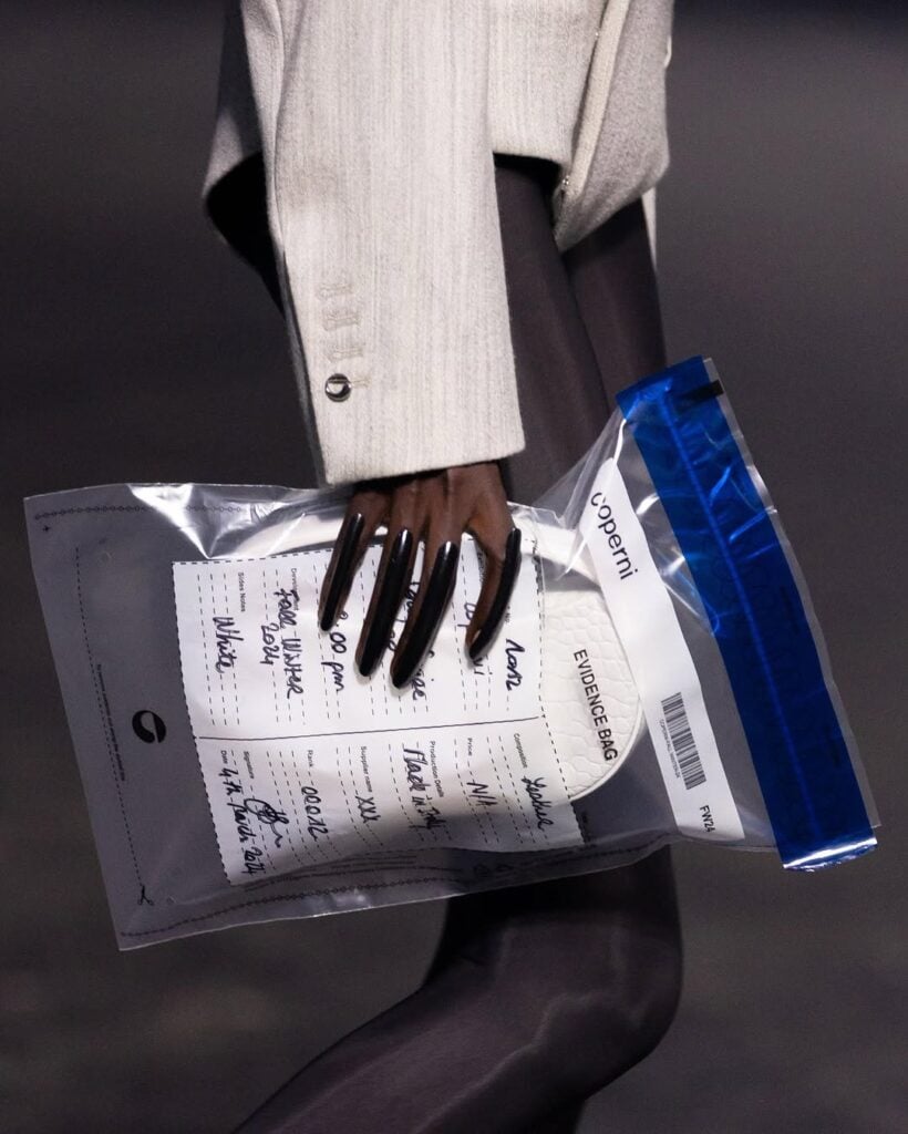 Mão de pele preta, com unha invertida, segurando uma bolsa da Coperni
