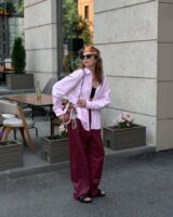 Mulher jovem e magra com calça vermelho-cereja, camisa rosa e chinelo preto.