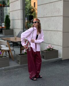 Mulher jovem e magra com calça vermelho-cereja, camisa rosa e chinelo preto.