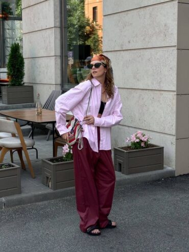 Mulher jovem e magra com calça vermelho-cereja, camisa rosa e chinelo preto.
