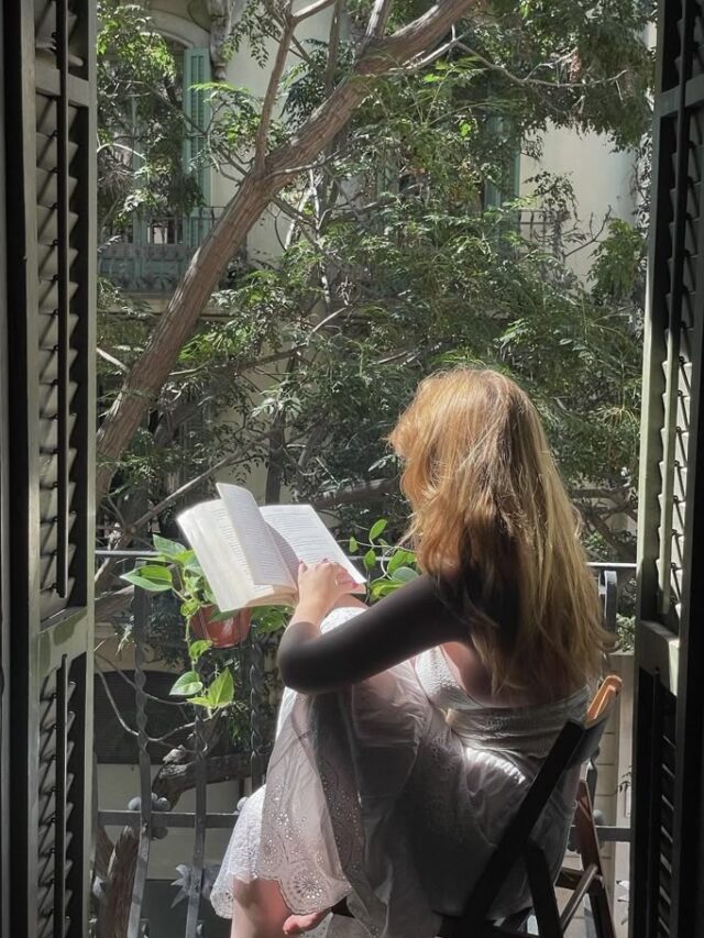 Mulher de pele clara, sentada na varando, lendo um livro