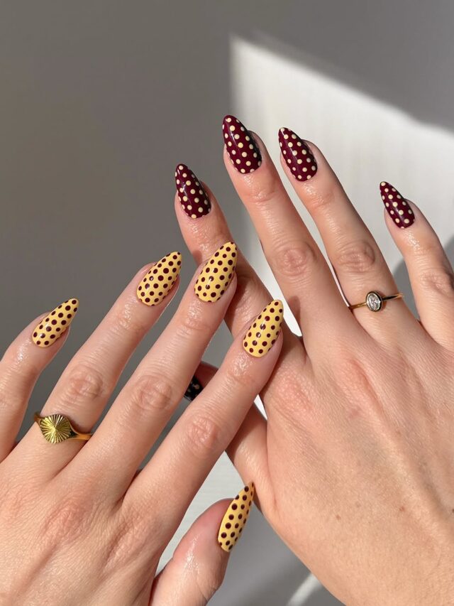 Mãos de pele clara, com anéis em dourado e unha com base amarela e marrom, com poá