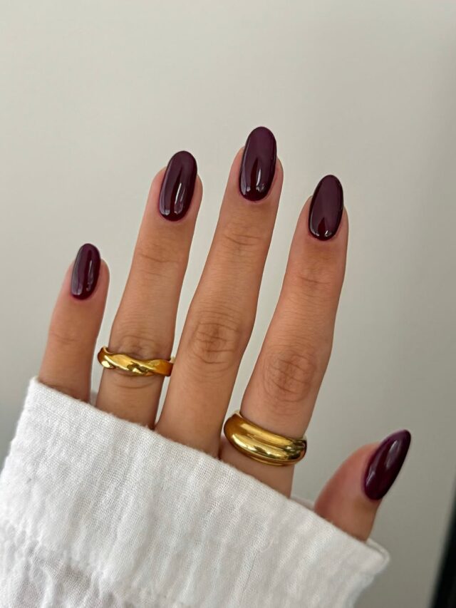 Mão de pele clara, com anéis em dourado e unha amendoada borgonha