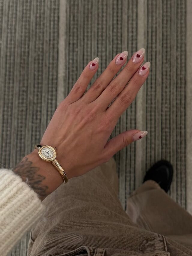 Mão de pele clara, com acessórios em dourado e unha dourada nude com coração vermelho