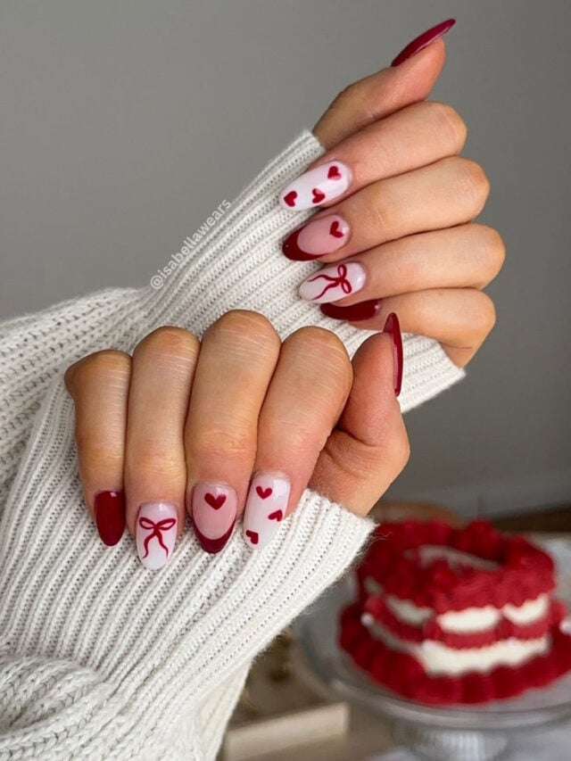 Mão de pele clara com mangas brancas de uma blusa de manga longa. As unhas são vermelhas com desenhos de coração e laços.