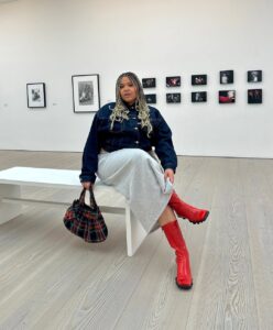 Mulher jovem midsize com look de outono composto de casaco jeans, saia de moletom e bota colorida.