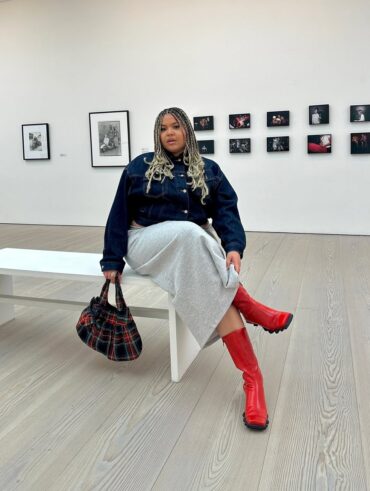 Mulher jovem midsize com look de outono composto de casaco jeans, saia de moletom e bota colorida.