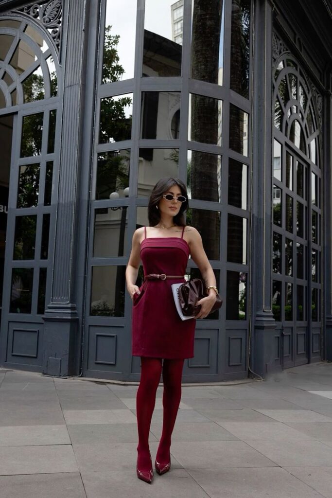 Mulher adulta com look monocromático composto de vestido, meia calça e salto alto.