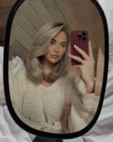 Mulher de pele clara, com suéter neutro e cabelo loiro médio