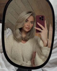 Mulher de pele clara, com suéter neutro e cabelo loiro médio