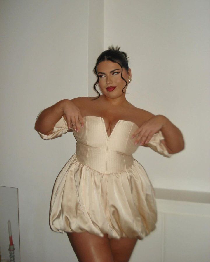Mulher jovem com corpo mid size. Ela usa vestido curto de modelo balonê.