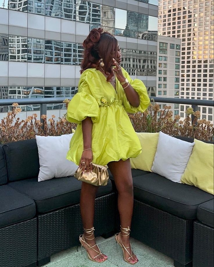 Mulher jovem de pele negra. Ela usa vestido verde limão com mangas bufantes e de comprimento curto.