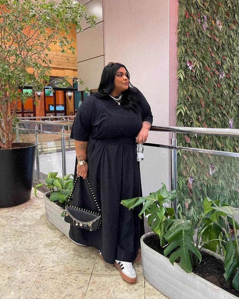 Mulher jovem de pele clara com vestido longo preto e tênis