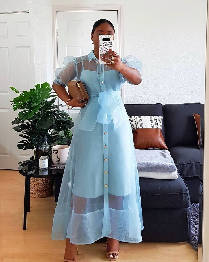 Mulher adulta com vestido azul. Ela tem pele escura e está com o cabelo preso.