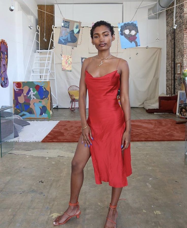 Mulher jovem de pele escura. Ela veste slipdress vermelho e sandálias vermelhas.