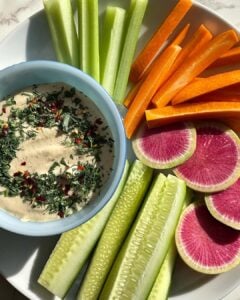 Verduras e frutas dispostas em um prato branco com um molho em uma cumbuca