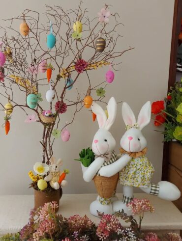 Casal de coelhinhos junto à árvore de páscoa com ovinhos e cenouras