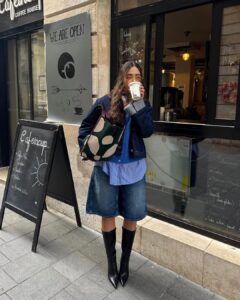 Mulher jovem com look com bermuda jeans e botas de cano longo