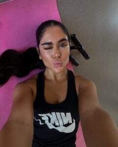Mulher de pele clara/médica, com look preto, cabelo preso e deitada na academia