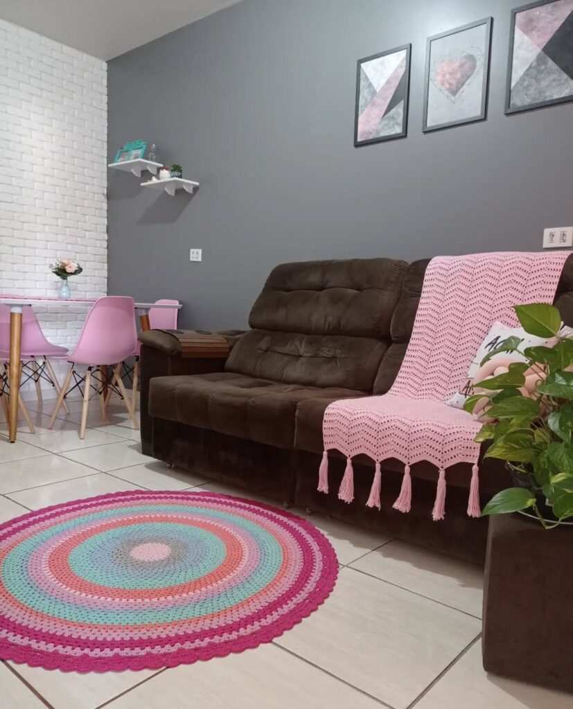 Sala com sofá marrom de veludo, manta rosa e tapete redondo de crochê