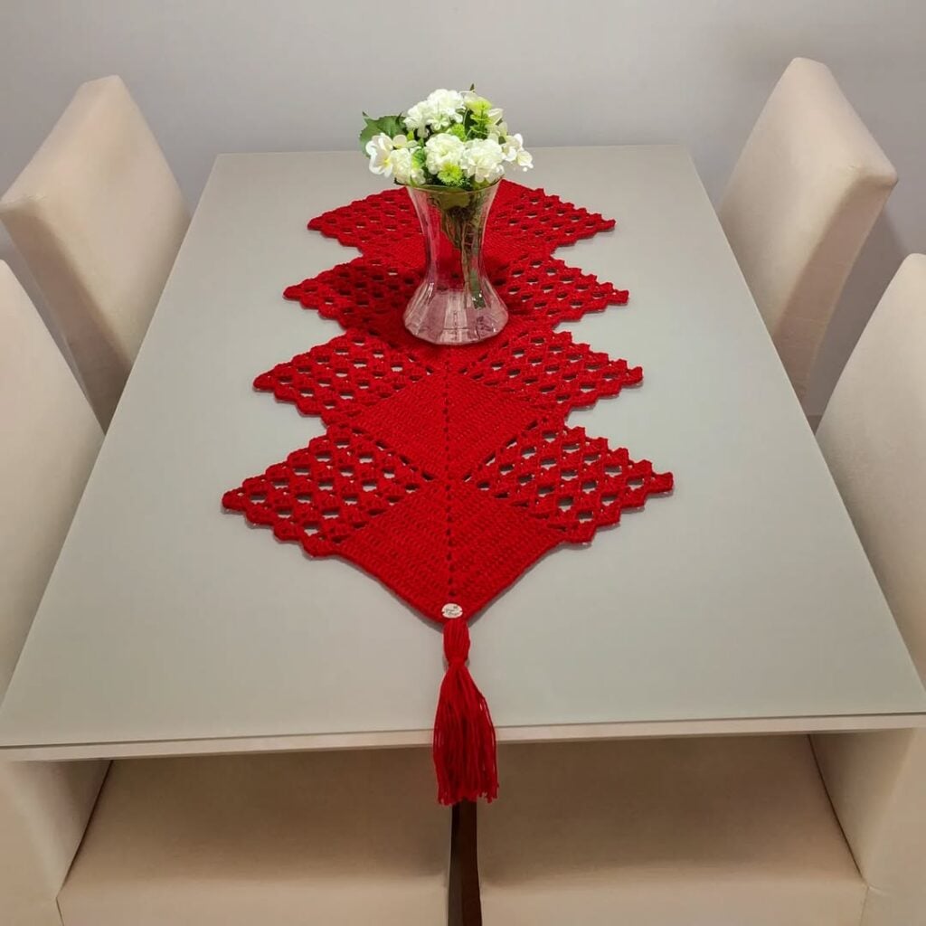 Trilho de mesa vermelho em crochê com vaso transparente e flores brancas