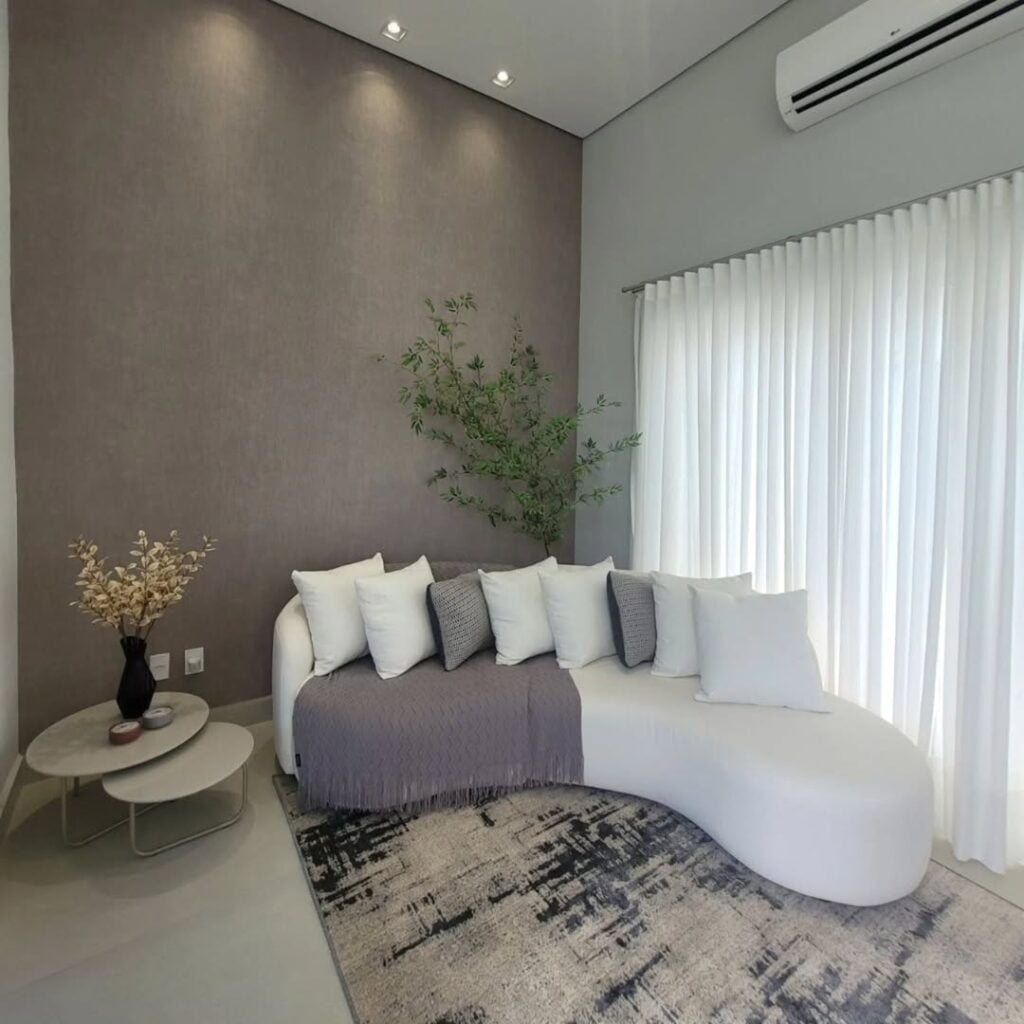 Sala com sofá branco de linhas curvas vom várias almofadas em cinza e branco