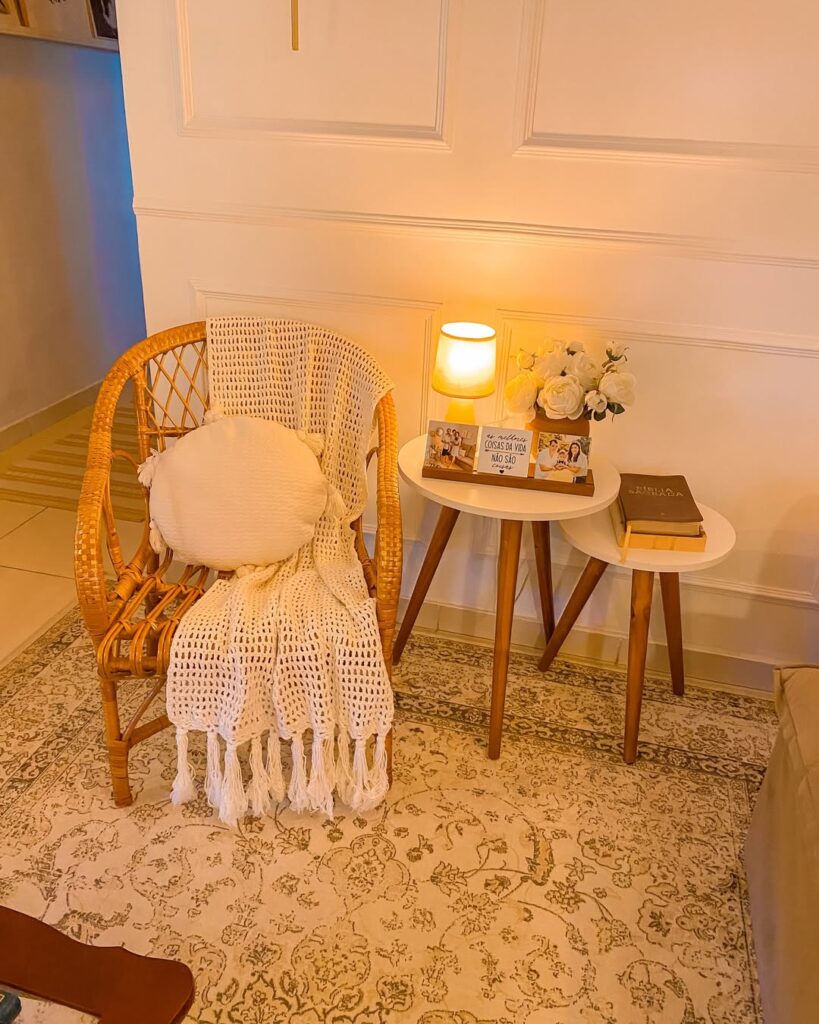Sala com cadeira de vime com manta e almofada bege, mesinhas de canto com abajur