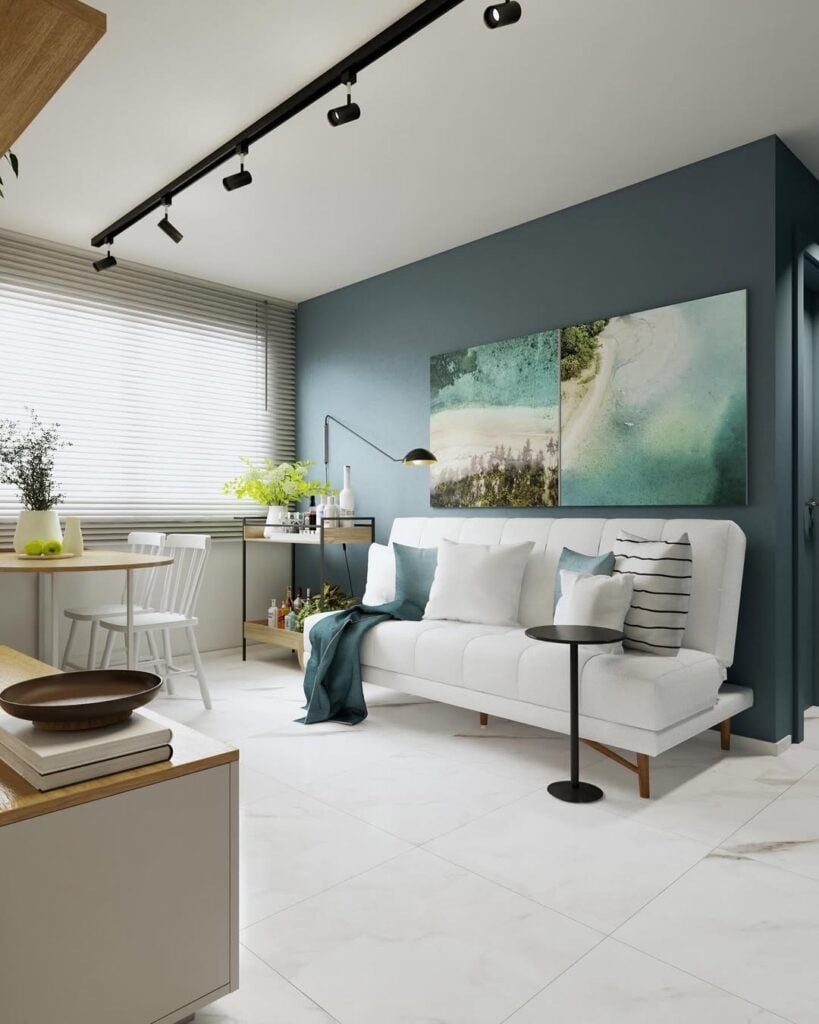 Sala de estar com sofá branco com pés de madeira, quadros na parede azul e mesinha preta
