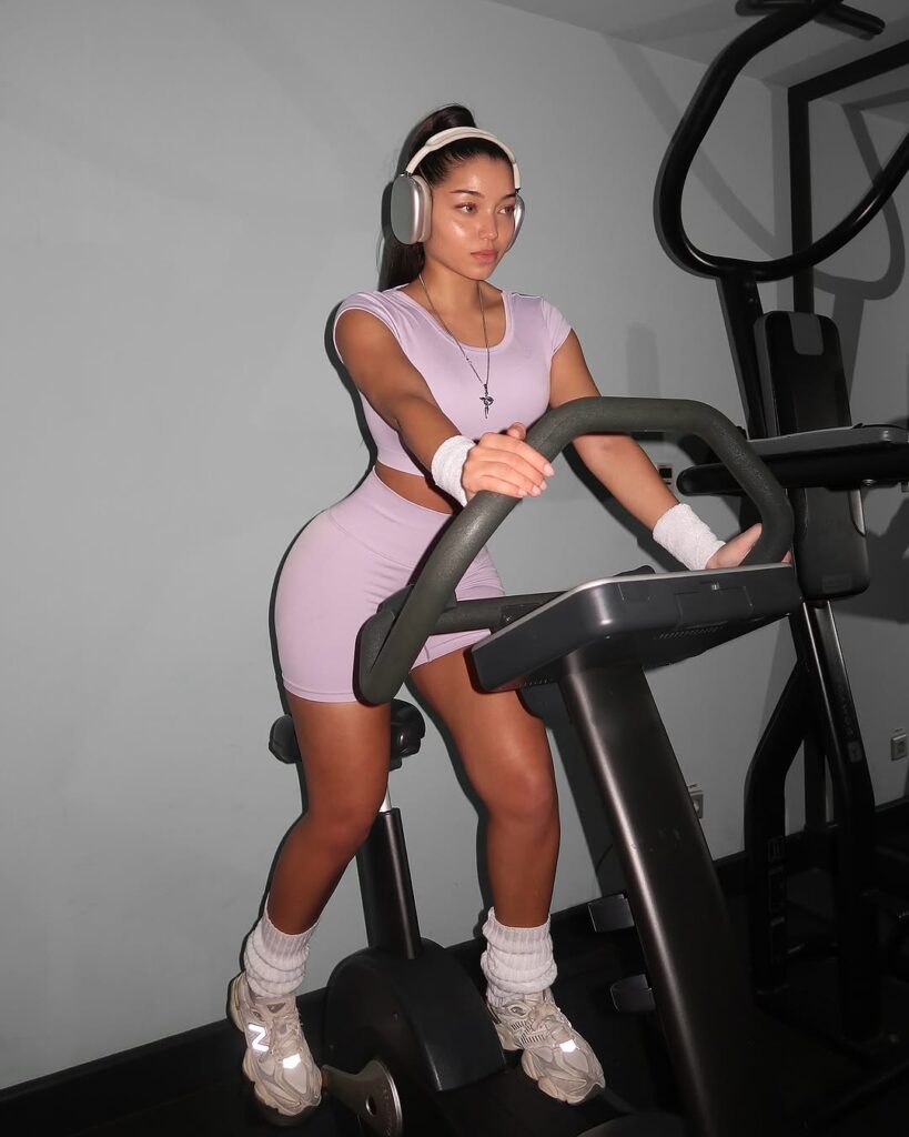Mulher de pele clara, com conjunto lilás. Ela está fazendo bike na academia