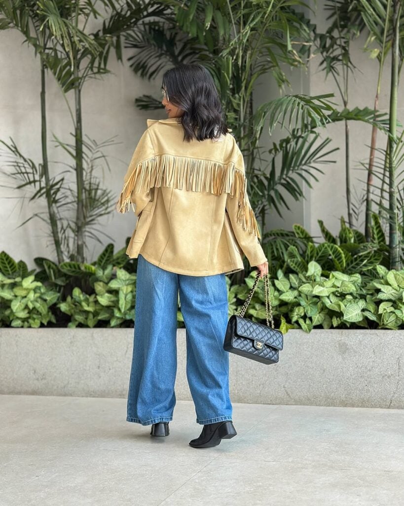 Mulher jovem virada de costas com jaqueta de franjas e calça jeans