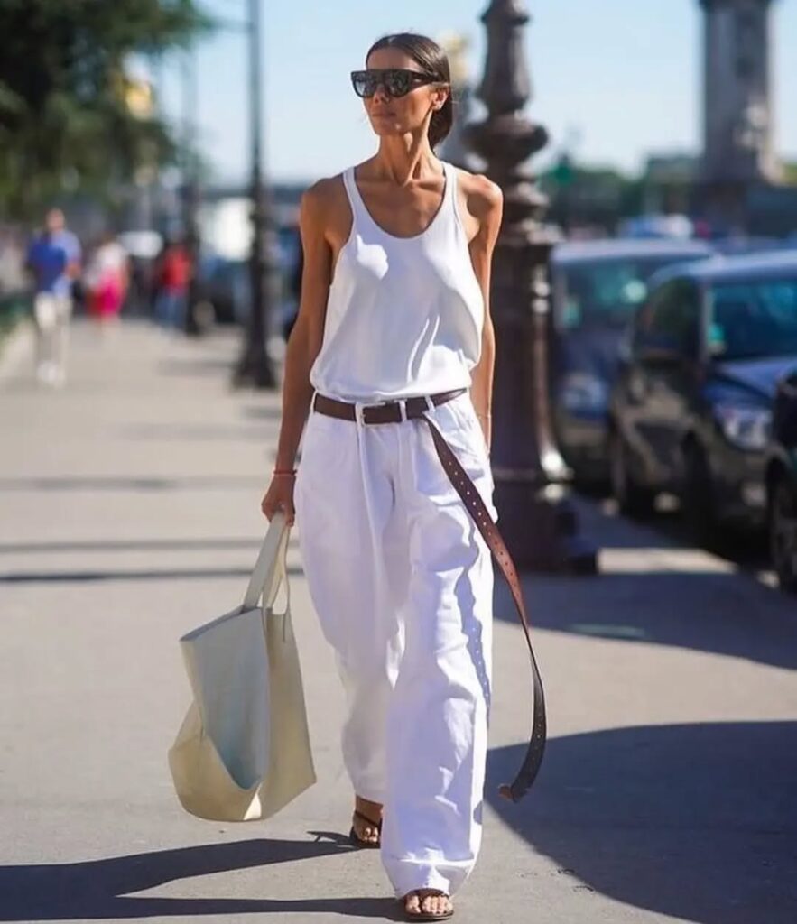 Mulher de pele clara, com cabelo preso, look all white e cinto longo