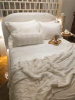 Quarto com cabeceira estofada e jogo de cama branco, com bandeja de bambu