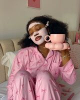 Mulher jovem de pele negra com pijama rosa e máscara facial rosa.
