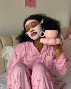 Mulher jovem de pele negra com pijama rosa e máscara facial rosa.