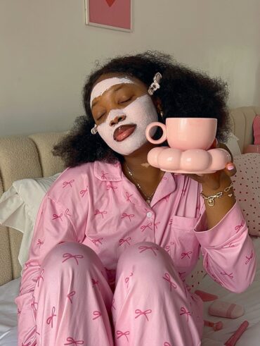 Mulher jovem de pele negra com pijama rosa e máscara facial rosa.
